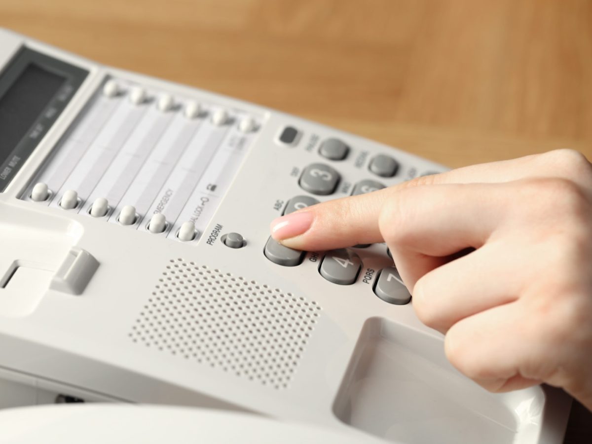 Finger pressing a number on a white desk phone