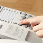 Finger pressing a number on a white desk phone