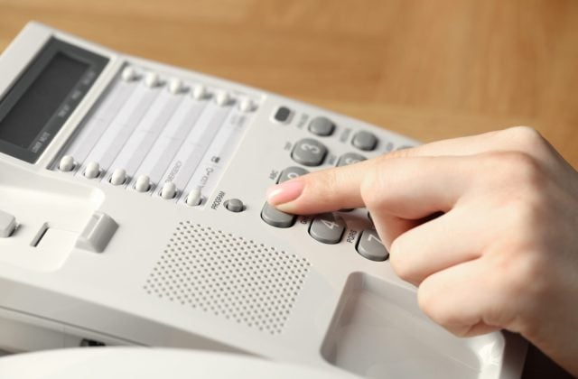 Finger pressing a number on a white desk phone